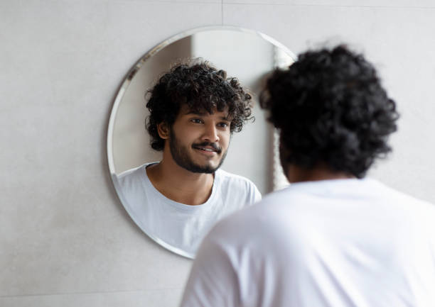 istock Handsome indian guy looking at his reflection in the mirror, standing in modern bathroom at home 1471775790