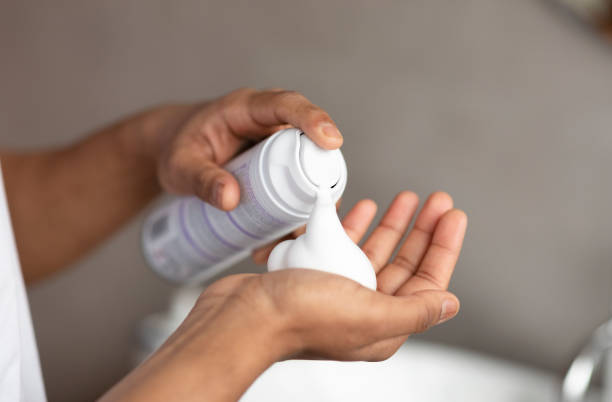 Unrecognizable man applying shave foam on hand, standing in bathroom and preparing for shaving, closeup