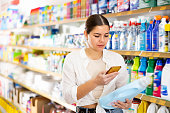 Girl scanning bottle of household detergent with smartphone