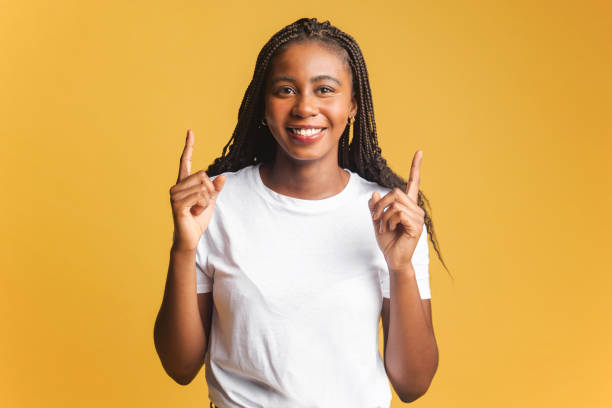 istock Friendly multiracial woman with Afro hairstyle points fingers up at empty space isolated on yellow background. Smiling female student advertising something 1471777508