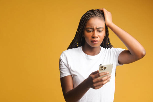 Shocked brunette young woman holding smartphone, looking at mobile phone screen and has disappointment face, received a bad news, made a mistake and a phone is locked stock photo