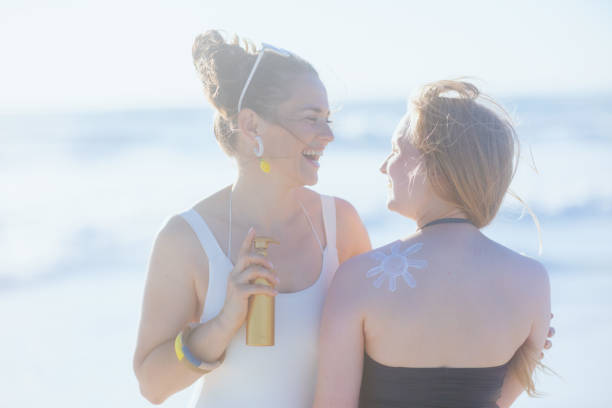 улыбающиеся стильные мать и ребенок на пляже с помощью солнцезащитного крема - teenager parent beach contemporary ст�оковые фото и изображения
