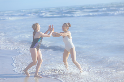 Full length portrait of happy modern mother and teenage daughter at the beach in beachwear having fun time.