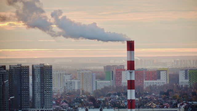 Smoke from a tall chimney over a winter city with houses in the snow, timelapse