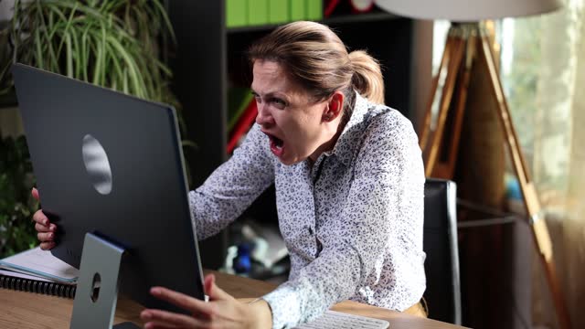 Angry business woman screaming into computer monitor at workplace