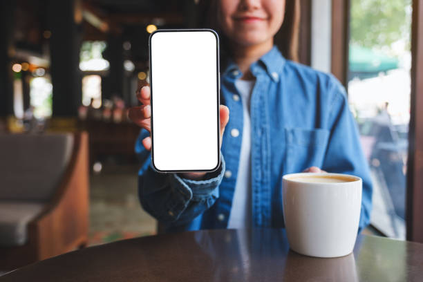 istock Mockup image of a woman holding and showing a mobile phone with blank white screen while drinking coffee in cafe 1471787556