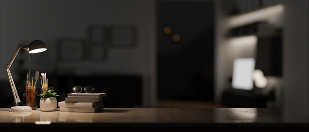 Close-up image of workspace tabletop with light from table lamp, book, decor plant, painting tools and copy space over blurred a dark room in background. 3d render, 3d illustration