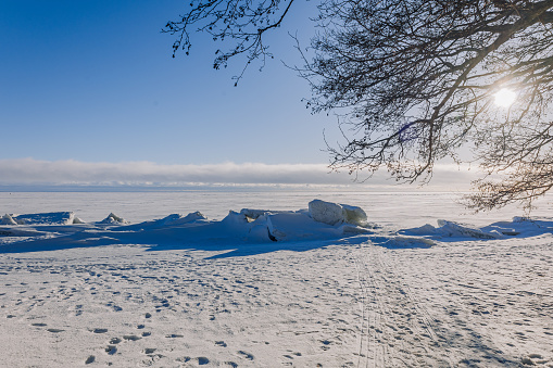 Winter landscape. Panoramic view of beautiful sunset on bay. Ice, snow and rocks on coastline. Setting sun in bright light. High quality photo