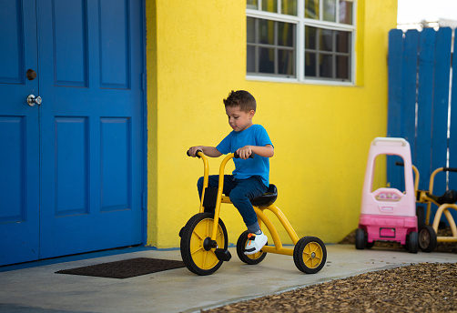 Hispanic boy playing on a daycare ridding a tricycle
