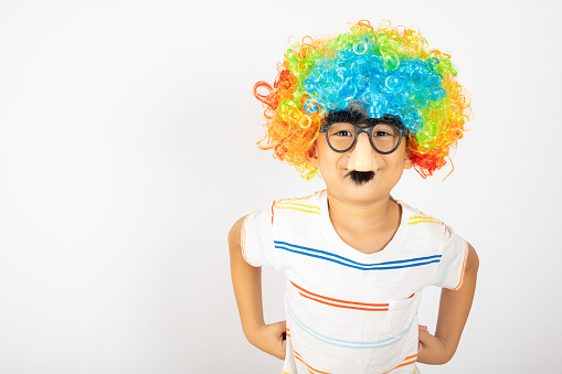 April Fool's Day. Portrait of Funny kid boy clown wears a curly wig colorful a big nos and glasses and has a mustache isolated on white background with copy space, Happy child festive decor