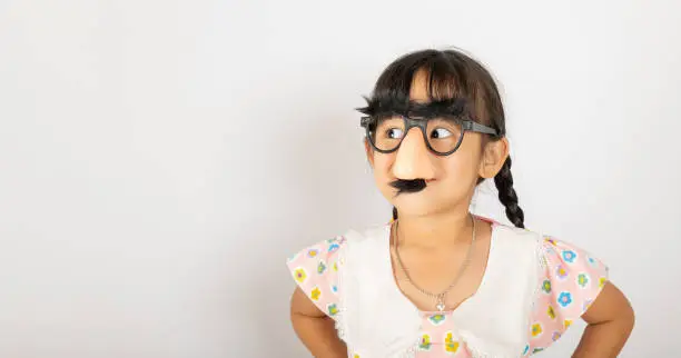 April Fool's Day. Portrait of Funny kid little girl clown wears a big nos and glasses and has a mustache isolated on white background with copy space, Happy smile child festive decor