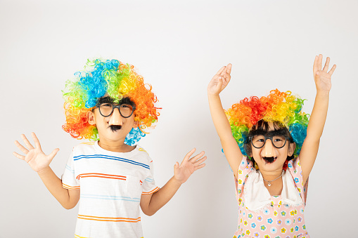 April Fool's Day. Two brothers funny kid little girl clown wears curly wig colorful big nos and glasses and has mustache playing fool isolated on white background copy space, Happy child festive decor