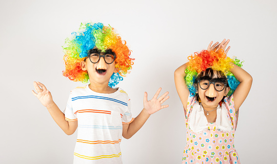 April Fool's Day. Two brothers funny kid little girl clown wears curly wig colorful big nos and glasses and has mustache playing fool isolated on white background copy space, Happy child festive decor
