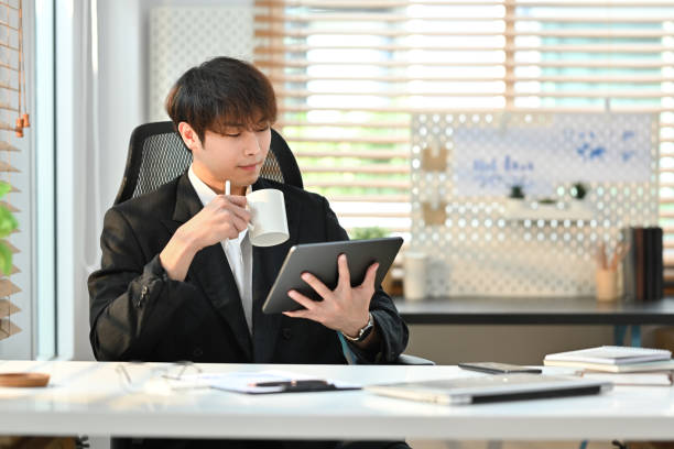 istock Handsome young businessman entrepreneur in formal wears drinking coffee and using digital tablet in his office. 1471813154