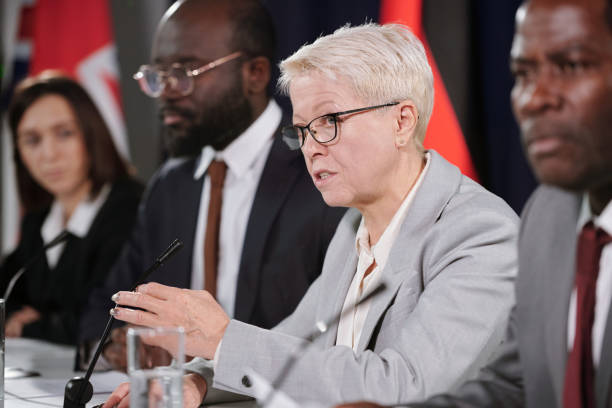 Mature female delegate talking in microphone among foreign colleagues