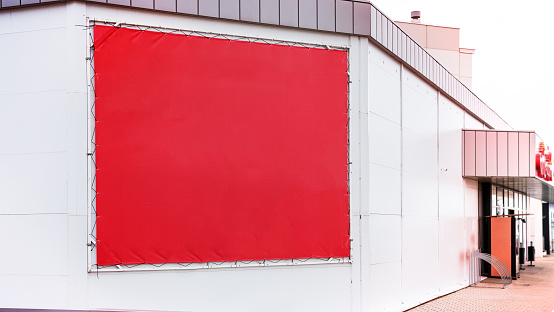 Empty red commercial vinyl banner mounted on supermarket wall outside. Blank poster with mockup space on building wall.