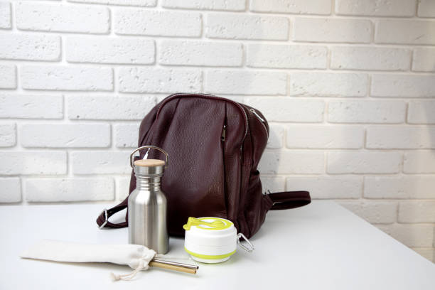 Eco friendly devices for drinks. A tin bottle for water and a collapsible silicone coffee mug near the bag stock photo