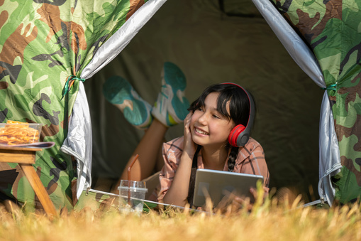 Young girl sleeps in tent and listens to music from tablet via Bluetooth to relax on holiday