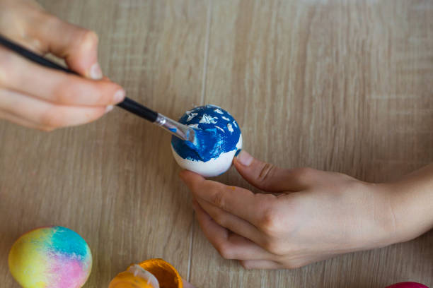 istock Children's hands close-up paint eggs with gouache. A girl paints Easter colored eggs with paints and a brush close-up. Easter. Spring. Painted eggs. The child decorates the eggs with gouache. The child celebrates Easter. 1471820013