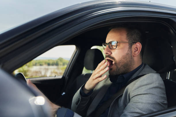 istock Tired businessman yawning while driving a car. 1471820352