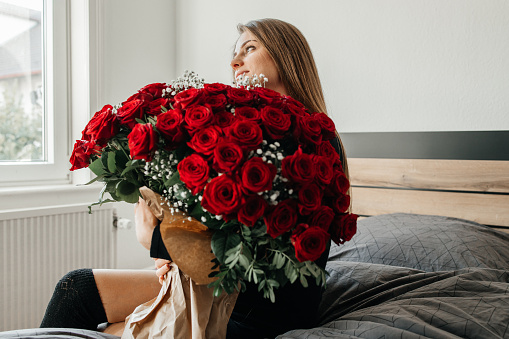 Charming young woman with a huge bouquet of red roses. Flower delivery for holidays and memorable dates.