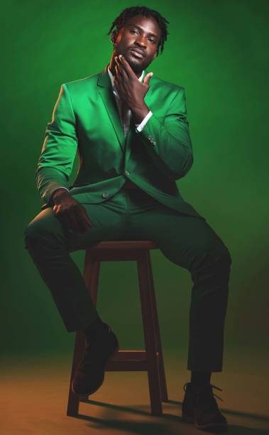 fashion, formal and portrait of a black man in a suit sitting on a chair in studio with a luxury outfit. elegant, stylish and african male model with fashionable clothes isolated by green background. - anti smoking imagens e fotografias de stock