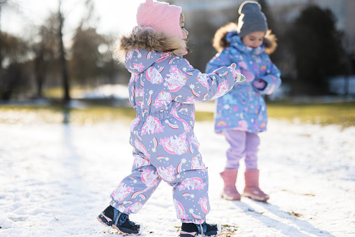 Two sisters in winter snowsuit playing together in sunny day.