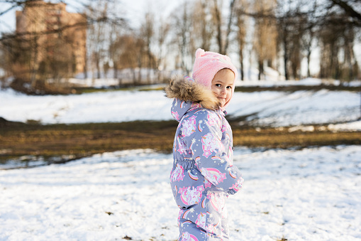 Baby girl in winter snowsuit in sunny day.