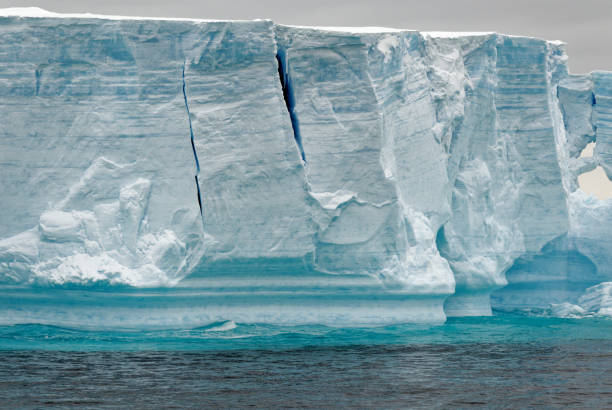 Massive flat topped iceberg floating in the Southern Ocean of Antarctica showing the weathered cracks, fissures holes and caves on the sides