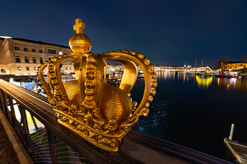 Famous place in Stockholm 1800s iron bridge featuring a gilded crown along a side railing & views of Gamla Stan Stockholm Old Town