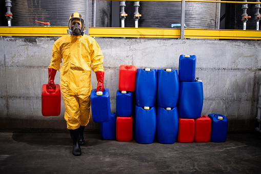 Chemical worker in protection suit and gas mask working in factory carrying dangerous material.