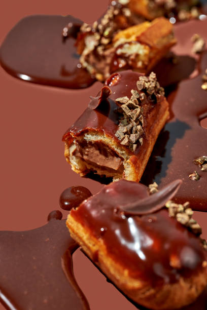 istock Art with an eclair. Broken eclair in puddles of icing on brown background. Conceptual monochrome food poster for pistachio profiteroles 1471828220
