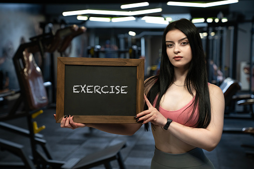 A profile view of a powerful young adult woman at the fitness center. Beautiful young sporty sexy woman showing a blackboard. Exercise message.