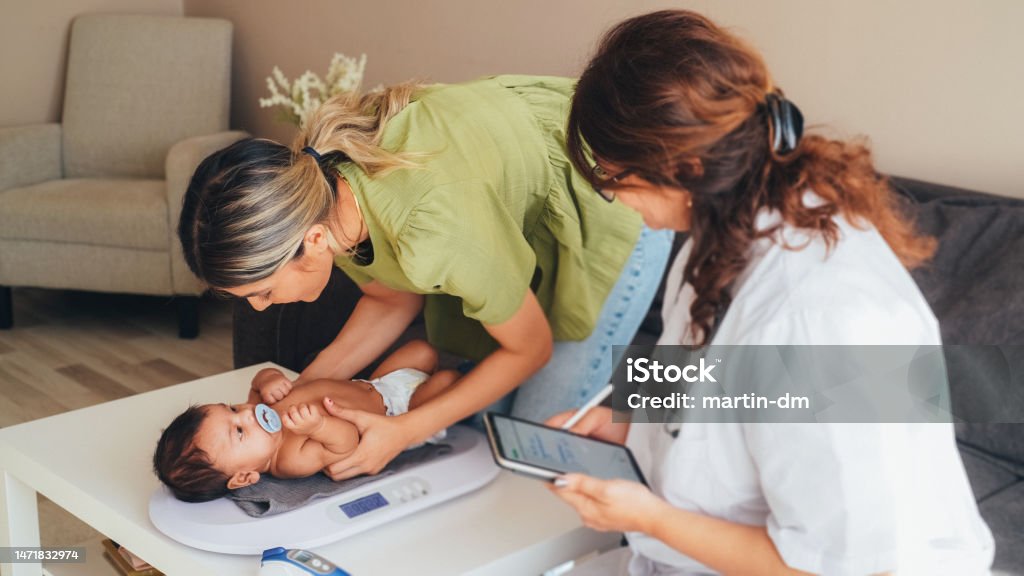Doctor visiting young mother at home for routine checkup of the newborn Midwife Stock Photo