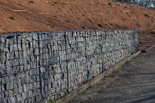 construction of a gabion retaining wall, as part of the house fencing. workers put geotextiles and on it wire baskets which consists of granite stones. demanding manual work, activity, geotextile, raster, landscaping, stabilization, landscaping