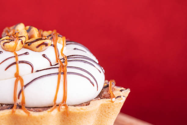 Delicious cupcakes with cream, caramel and nuts, on red background, macro shot