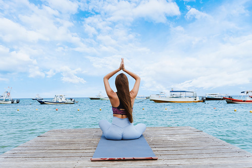 Young hispanic woman practicing yoga on the beach pier or dock at the seaside in Mexico Latin America