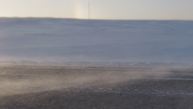 Handheld shot of snow particles blowing in the wind over a road