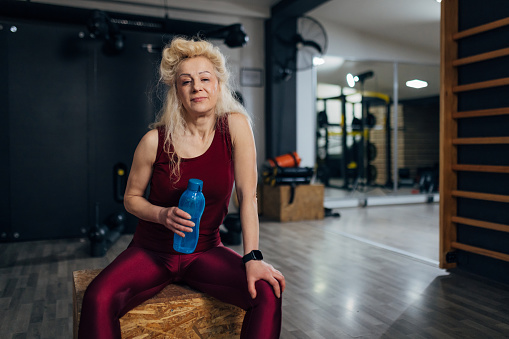 Portrait of a confident middle-aged woman sitting on a box at the gym and looking directly into the camera