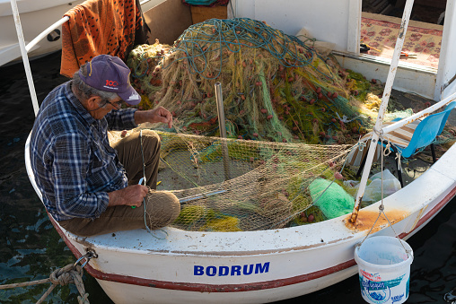 Bodrum, Mugla, Turkey. April 23rd 2022\nA fisherman mending nets on his boat in Bodrum town harbor, the Aegean seaside location in Turkey is a popular Turkish tourism destination