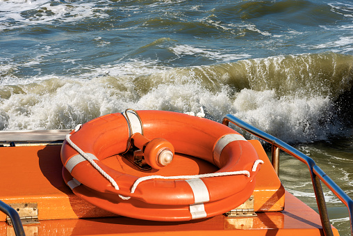 Orange life buoy with an emergency light for localization over a boat with a rough sea on background.
