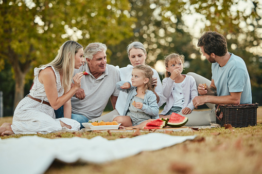Happy family, park picnic and summer with fruit, eating and love in nature, holiday and bonding in spring. Big family, healthy watermelon and kids with mom, dad and grandparents on lawn in Melbourne
