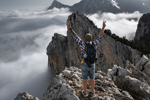 On the top of the mountain. Successful climb to the top of the mountain. Tourist watches mountain peaks with arms raised above beautiful clouds