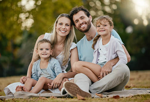 Family, park picnic and portrait with smile, love and happiness for bonding on blanket, grass and sunshine. Young happy family, lawn and parents with kids, trees and relax together for summer holiday