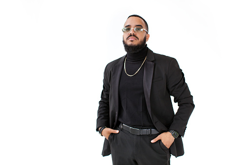 Fashion style portrait Fashionable arab business man with beard and mustache in black suit with jacket and turtleneck, wears glasses, chain, watch and belt isolate on white background