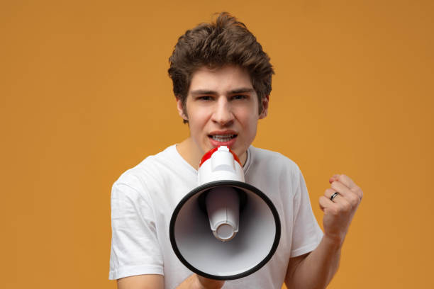 istock Young man shouting into megaphone making announcement against yellow background 1471844009