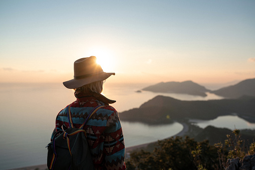 Woman in modern clothing and hat watching sunset standing on the top of the mountain. Oludeniz Beach, Turkey