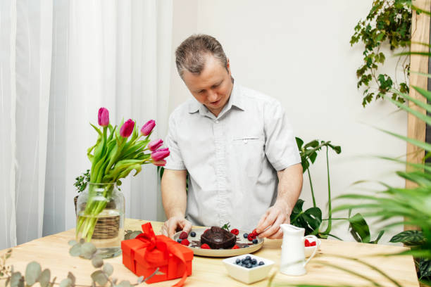 A man decorates a chocolate cake heart with fresh berries and chocolate icing. Present, surprise for Valentine's Day or Mother's Day, Women's Day.