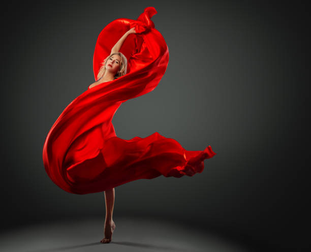 bailarina dançando com tecido de seda vermelha voando no vento. bailarino moderno saltando sobre o fundo do dark studio. mulher da moda no vestido vermelho envolto no lenço ondulante - women dancing contemporary red - fotografias e filmes do acervo