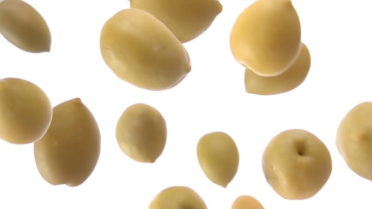 Super close-up of fresh green olives falling diagonally on the white background